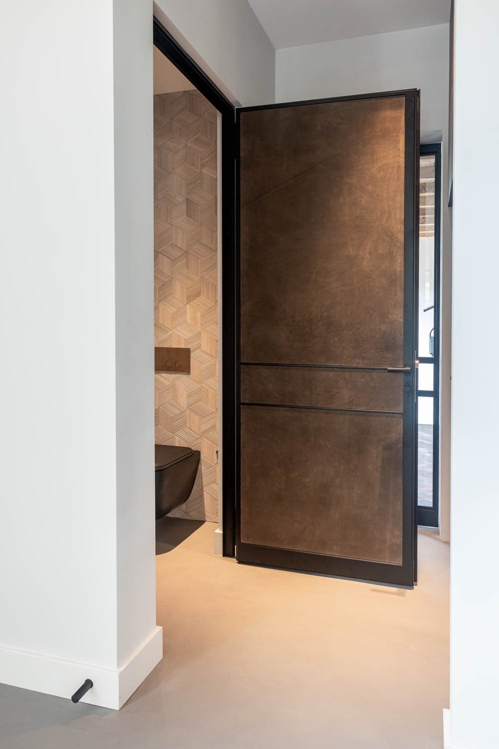 a hinged steel door with leather panels seen in a powder room